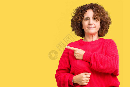 美丽的中年高级女红色冬季毛衣在孤立的背景下用手指着侧面展示广告图片