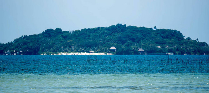 一张盛暑炎热日以蓝水和绿岛为背景的海滩图片