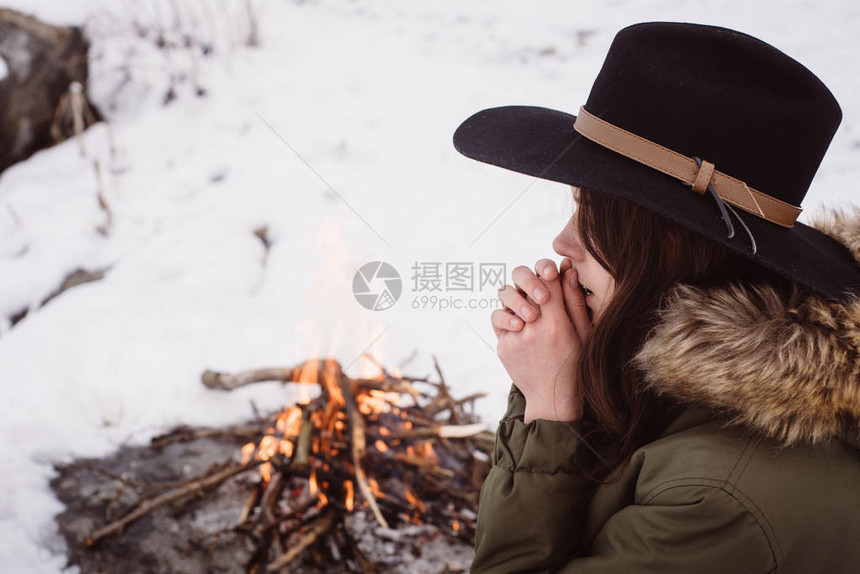 戴帽子的女孩在寒冷湖背景的冬季灾附近用温暖的手亲热图片