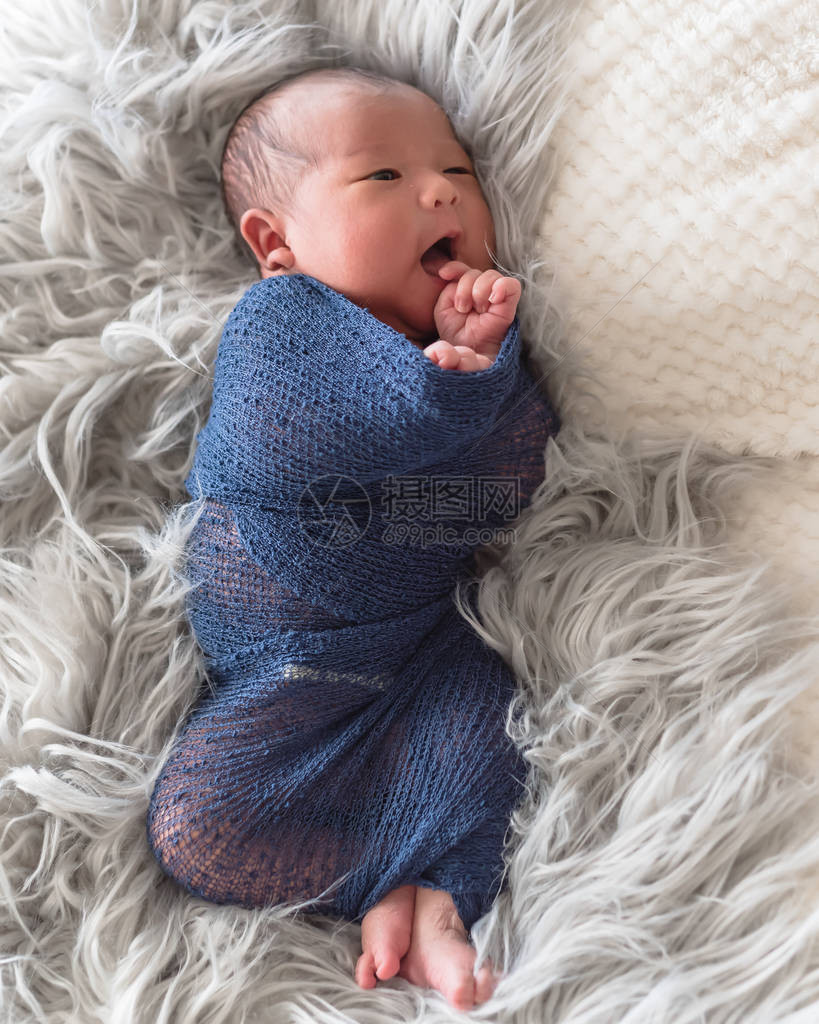 可爱的亚洲新生婴儿男孩被披着长毛毯裹在地毯上的紫编织的摩海发包中卷起来图片