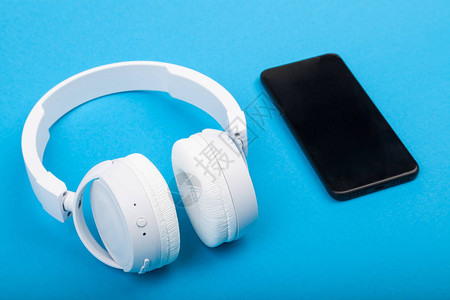 手持无线白色耳机的智能手机在蓝背景图片