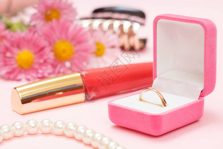 盒子里的金戒指珠子口红头发和粉红色背景的鲜花图片