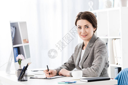 穿着灰色西装的有吸引力的女商人与电脑坐在桌边图片