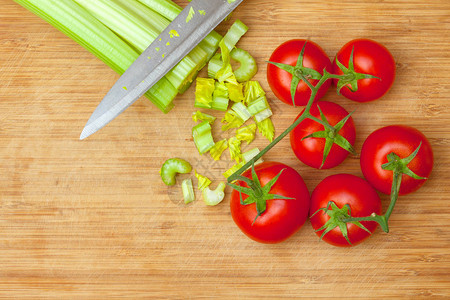 铁刀旁木砧板上的芹菜和红番茄的绿色茎图片