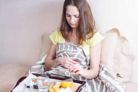 患有头痛和感冒的妇女与温度计一起在床上使用平板药和维生素治疗图片