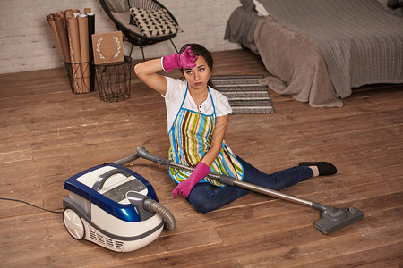 一位年轻的家庭主妇坐在厌倦了家务的吸尘器上在家做务情绪图片