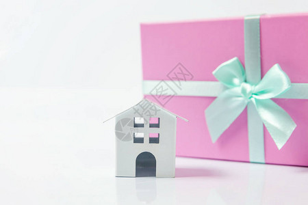 微型白色玩具屋和礼品盒包装在白色背景上的粉红色纸图片