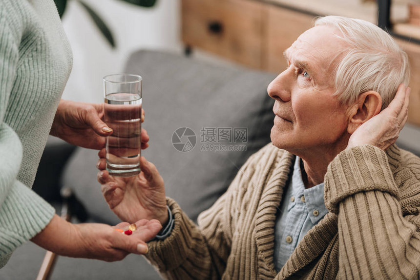 老人从丈夫那里拿一杯水和药丸图片