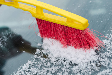 用红色和黄色刷子从雪中清洗车挡风玻璃的过程图片