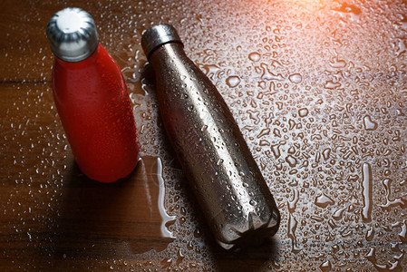 两瓶不锈热瓶放在木制桌子上喷洒水雾图片