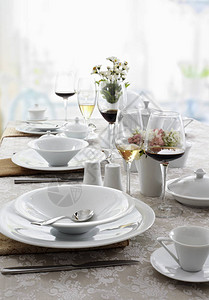 提供白色菜肴餐具和酒杯的餐桌图片