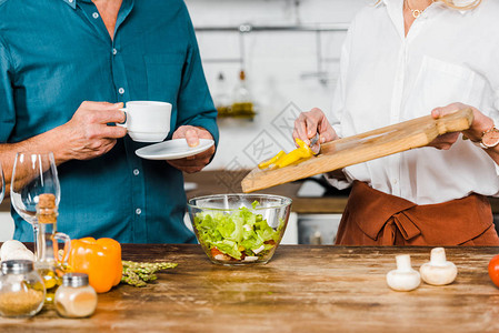 成熟妻子把蔬菜放碗里和丈夫在厨房端茶杯的成熟妻图片