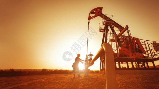 石油工人正在检查日落的油井附近的水泵背景图片