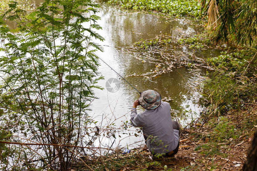戴帽子的男人正在一个小池塘里钓鱼图片