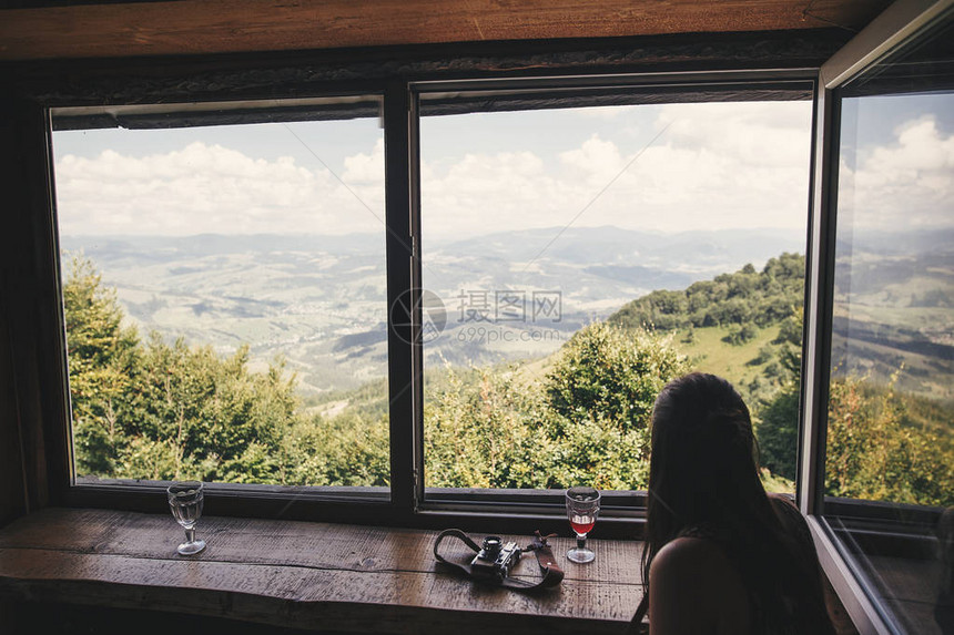 时尚的时髦女孩透过旧小屋的大窗户望着山顶放松在夏天山的少妇旅行和旅行癖惊图片