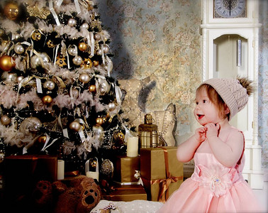 穿着毛发粉红服装和帽子的可爱小姑娘在新年树缝合处图片