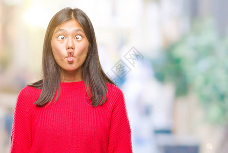 穿着冬毛衣的年轻亚洲女人在孤立的背景之下用嘴唇疯狂和滑稽的手势做鱼脸图片