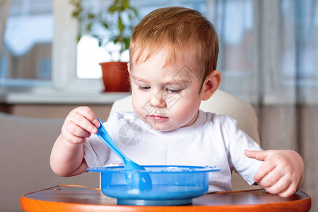 小男孩在厨房的儿童餐桌旁用勺子自己吃饭健康婴图片