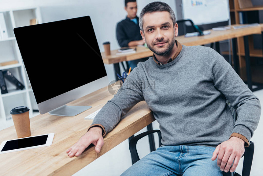 英俊男子在用台式计算机和办公室数字平板电脑坐在桌图片