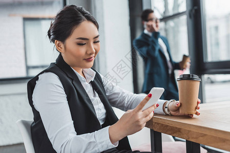 拥有咖啡和在工作场所使用智能手机的Kazakh女商业妇女图片