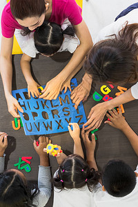 亚洲教师与亚洲学生一起玩彩色字母拼图游戏图片