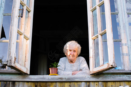 老妇人从村屋的窗户望去图片