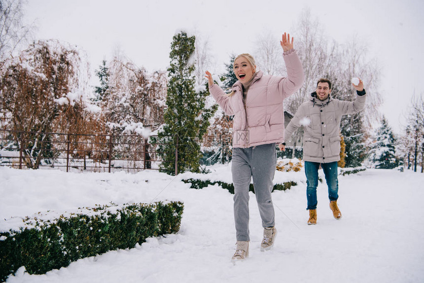 欢快的女子逃离男朋友在冬天扔雪球图片