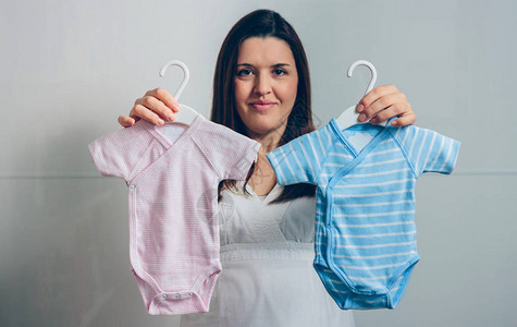 孕妇在室内露出粉红和蓝色婴儿体服图片