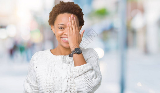 美丽的年轻非洲裔美国女人穿着毛衣在孤立的背景下用手捂住一只眼睛图片
