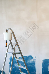 用手锤和白色桶涂在建筑墙上的背景壁上进行更高工作的楼梯的垂直相照图片