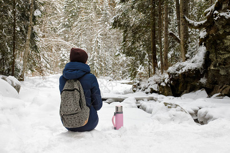 背着包和热水瓶的女孩坐在雪图片