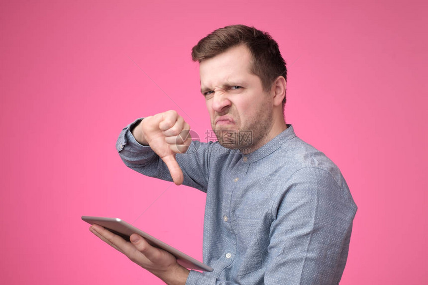 年轻的欧洲嬉皮士男子做坏信号显示拇指下手握着平板电脑他有坏消息或者在互联网上读到图片