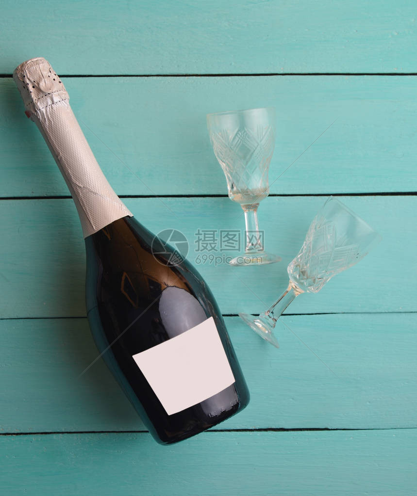 一瓶香槟和两杯倒影眼镜在蓝色木制桌图片