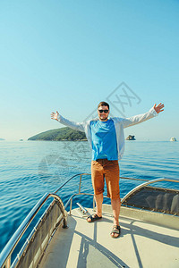 成功男子站在船的鼻子上有海和山在背图片