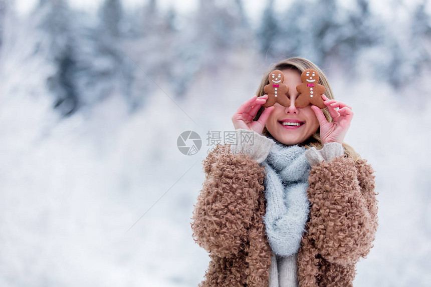 穿着大衣的漂亮女孩在雪林里吃饼干情人节圣图片