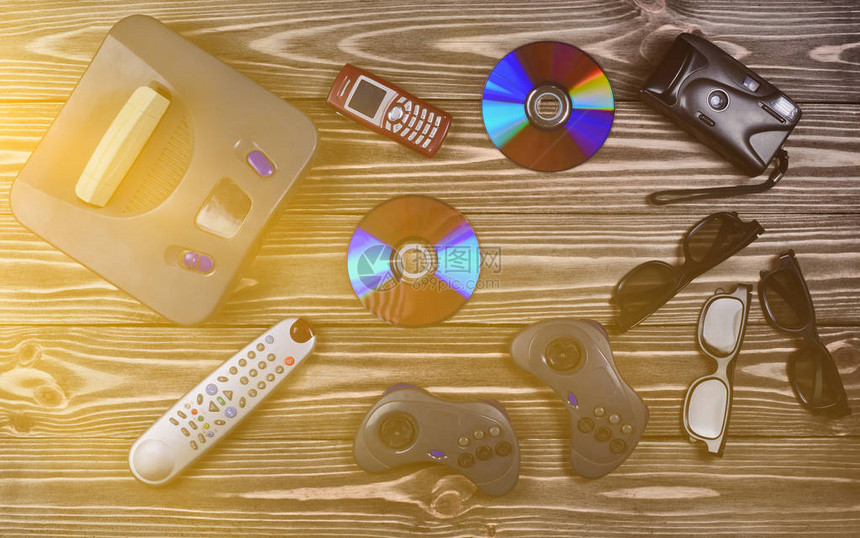 老式媒体和信息技术娱乐90年代游戏机游戏手柄磁盘电话木桌上的胶卷相机图片