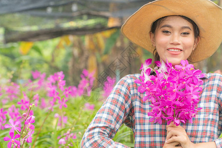 一位身穿格子衬衫戴着帽子的女园丁手里拿着一朵粉红色的兰花并且笑得很开图片