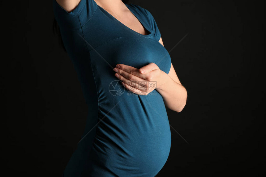 孕妇在深色背景下抚摸她的乳房图片