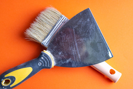 金属刮刀带塑料手柄的抹子和白色背景上的两个油漆刷图片