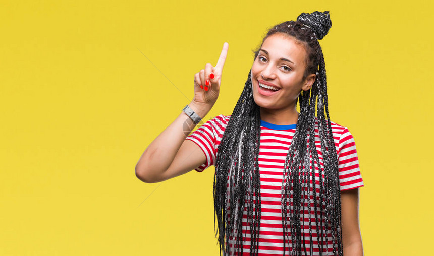 年轻的编织头发非洲裔美国女孩在孤立的背景下展示并用第一号手指向上方图片