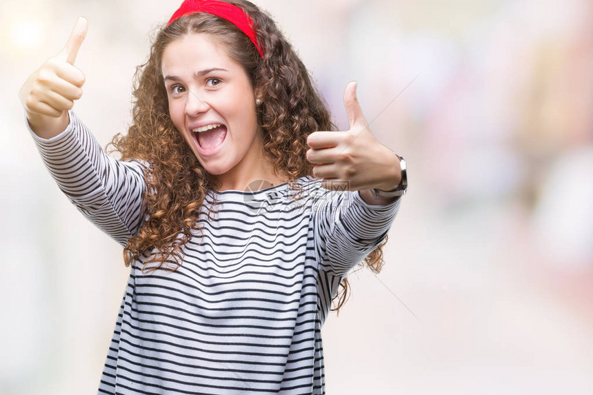 美丽的黑发卷年轻女孩穿着条纹毛衣在孤立的背景下批准用手做积极的手势图片