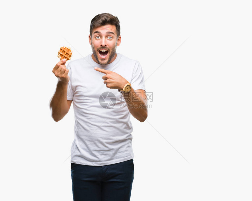 英俊的年轻帅哥在孤立的背景中吃甜美的华夫饼非常快乐地用图片