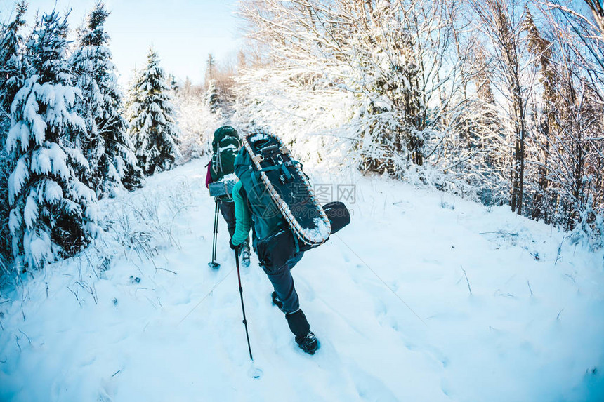 两名妇女在冬季远足带着登山杖的女朋友在白雪覆盖的山路上背包和雪鞋的女孩一起旅行朋友们在阳光明媚的日子图片