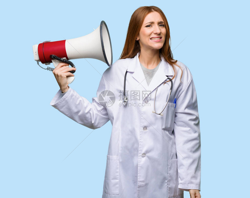 红头女医生用扩音器在孤立的蓝色背景下发出声响图片