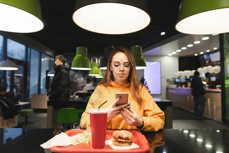 女孩用智能手机在快餐店吃饭图片