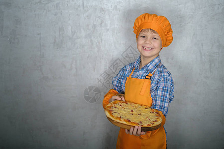 身着厨师服装的欧洲男孩拿着新鲜准备的土制披萨图片