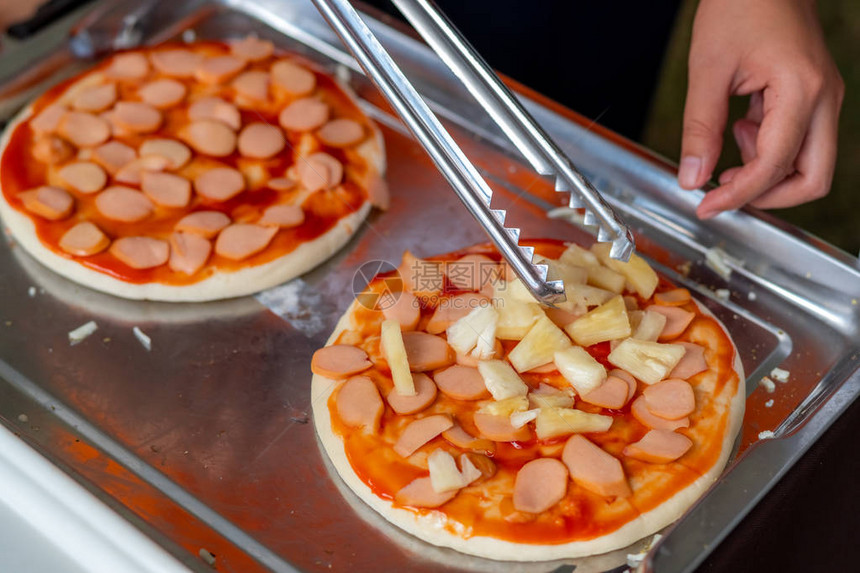男人用比萨饼皮和菠萝做比萨饼捐赠慈善活动女厨师用手将比萨饼的配料放在木桌上的托盘中准备比萨图片