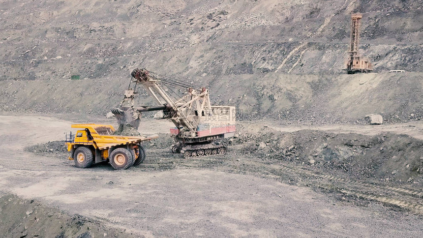 在灰色采石场采矿业装载石矿时的挖掘机和自卸车重型采矿挖掘机将岩石矿装入翻斗式大型采矿卡车图片
