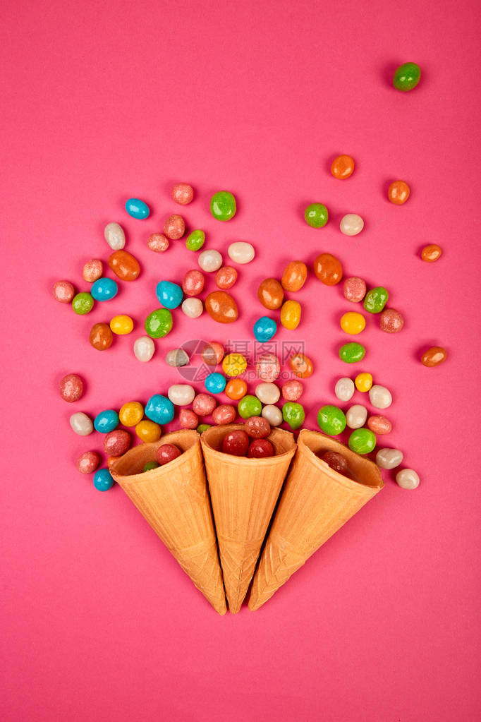冰淇淋华夫饼锥与五颜六色的糖果糖果冻散落在粉红色背景上的五彩糖果图片