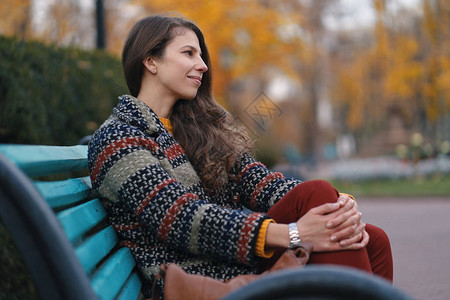 心情不错的年轻美女在秋天摆出姿势坐在长椅上享受好天气图片